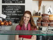 Bediener lächelt hinter Bäckertheke — Stockfoto