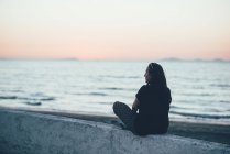 Задній вид жінка сидить на стіні, дивлячись на океан, Sorso, Сассарі (Італія) — стокове фото
