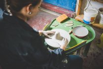 Sopra la spalla vista di giovane donna seduta con ruota in ceramica — Foto stock