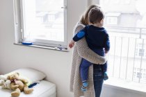 Rear view of mid adult woman and baby son looking through window — Stock Photo