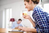 Young woman in blue checked shirt eating an apple and using a tablet — Stock Photo