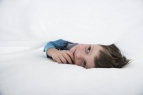 Junge liegt zwischen weißen Bettlaken — Stockfoto