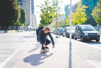 Giovane skateboarder maschile accovacciato mentre skateboard sul marciapiede — Foto stock