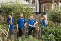 Porträt von vier Schulkindern mit Gartengeräten im Garten — Stockfoto
