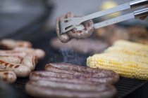 Barbecuing sausages and corn on the cob — Stock Photo