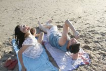 Portrait of young couple on towels on beach looking up — Stock Photo