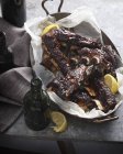 Dish of roasted beef ribs with lemon slices and bottles on table — Stock Photo