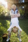 Madre levantando hija al revés en el jardín - foto de stock