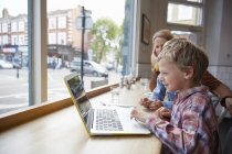 Niño pequeño usando el ordenador portátil en la cafetería, Londres, Reino Unido - foto de stock