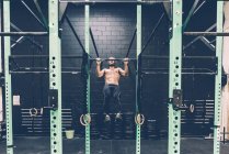 Young male cross trainer doing chin ups on exercise bar in gym — Stock Photo
