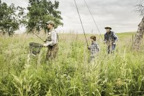 Multi generation family in field carrying fishing rods and fishing net — Stock Photo
