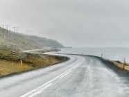 Vista panorámica de la sinuosa carretera costera húmeda, Hof, Islandia - foto de stock