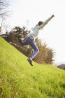 Jeune garçon sautant dans un champ herbeux escarpé — Photo de stock