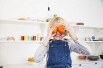Portrait of cute girl in kitchen holding oranges to her eyes — Stock Photo