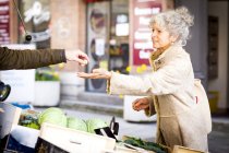 Mature female shopper buying vegetables at local french market — Stock Photo