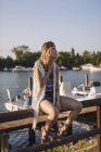 Блондинка кавказька жінка сидить на паркані біля озера вода з човнами і яхтами — стокове фото