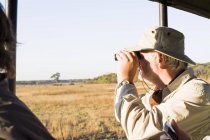 Senior man looking out through binoculars on safari, Kafue National Park, Zambia — Stock Photo