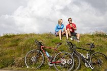 Cyclists relaxing and chatting on grassy hilltop — Stock Photo