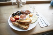 Assiette de petit déjeuner avec œufs frits, saucisses, champignons, tomates et toasts — Photo de stock