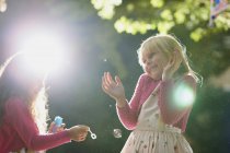 Duas meninas soprando e estourando bolhas no jardim iluminado pelo sol — Fotografia de Stock