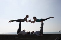 Silhouette simmetriche uomini e donne che praticano yoga acrobatico a parete sulla spiaggia di Brighton — Foto stock
