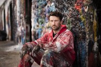 Portrait of male ship painter sitting against paint splattered wall — Stock Photo