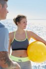 Woman in front of ocean holding yellow ball looking away smiling — Stock Photo
