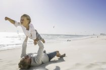 Отец лежит на пляже, поднимая сына — стоковое фото