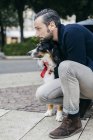 Metà uomo adulto accovacciato con cane da compagnia sul marciapiede della città — Foto stock