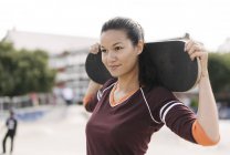 Портрет женщины-скейтбордистки со скейтбордом на плечах — стоковое фото