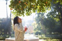 Seitenansicht der reifen Frau bläst Blasen unter Orangenbaum, Sevilla, Spanien — Stockfoto