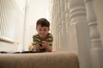 Boy lying at staircase playing with toys — Stock Photo