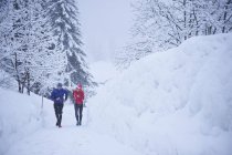 Hombre y mujer corriendo en el bosque cubierto de nieve, Gstaad, Suiza - foto de stock