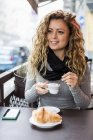Жінка в кафе тримає чашку еспресо, дивлячись геть посміхаючись — стокове фото