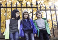 Three boys outdoors, leaning against fence, low angle view — Stock Photo