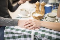 Cropped view of couple holding hands at cafe table — Stock Photo