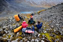 Cuatro excursionistas adultos tomando un descanso en el paisaje del valle escarpado, montañas Khibiny, península de Kola, Rusia - foto de stock