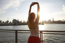 Rear view of woman on pier arms raised stretching, Manhattan, New York, USA — Stock Photo