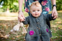 Portrait of baby girl holding mother's hands and toddling in park — Stock Photo