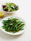 Close-up view of plate of roasted asparagus on table with salad bowl — Stock Photo