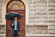 Uomo d'affari che trasporta ombrello in strada — Foto stock