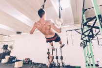 Visão traseira do treinamento de treinador cruzado masculino em anéis de ginástica — Fotografia de Stock