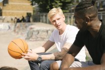 Dos jóvenes jugadores de baloncesto chateando en el parque de skate de la ciudad - foto de stock