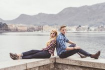 Portrait de jeune couple assis dos à dos sur le mur du port, Lac de Côme, Italie — Photo de stock