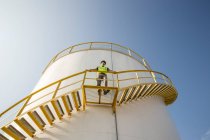 Male worker standing on steps of storage container at fuel depot, low angle view — Stock Photo