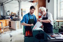 Senior Handwerker / Techniker betreut jungen Mann auf Buchdruckmaschine in Buchkunstwerkstatt — Stockfoto