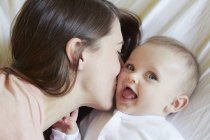 Portrait of cute baby girl being kissed by mother on bed — Stock Photo