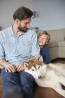 Father and son sitting with dog face to face smiling — Stock Photo