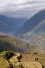 Rainbow over rural mountain valley in sunlight — Stock Photo