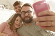 Hombre adulto medio y dos niños tomando selfie smartphone - foto de stock